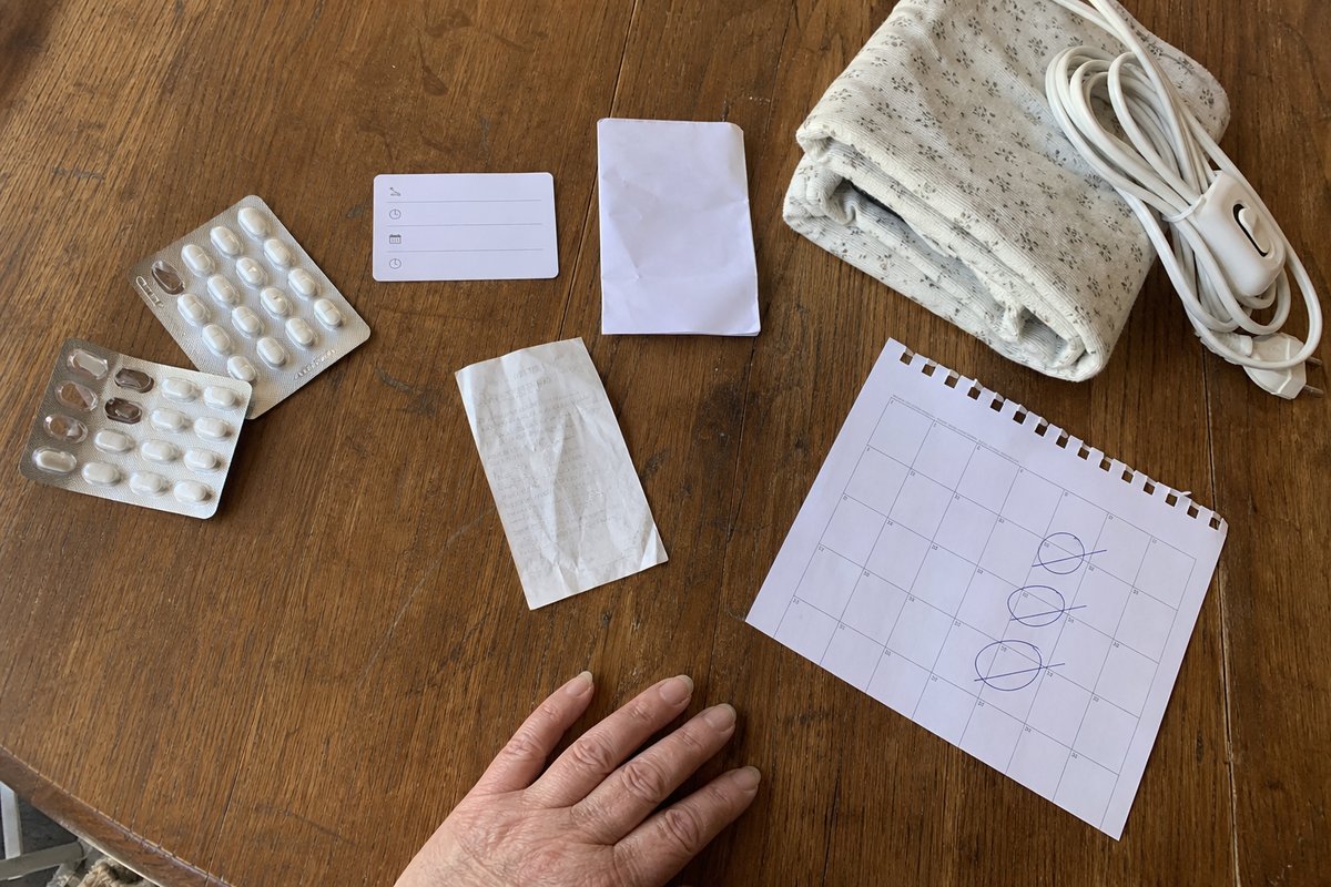 Køkkenbord med smertestillende, fysioterapikort, blokade-kvittering og varmepude arrangeret sammen